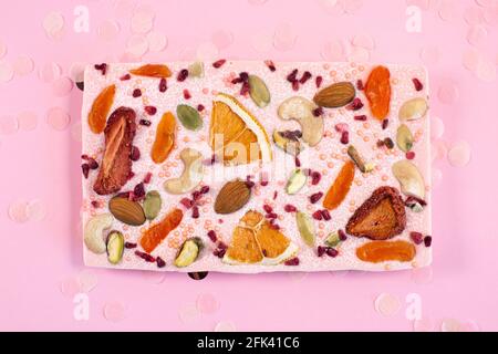 Handmade pink chocolate bar with dried fruits and nuts on a fastive Pink Background. Greeting card concep Stock Photo