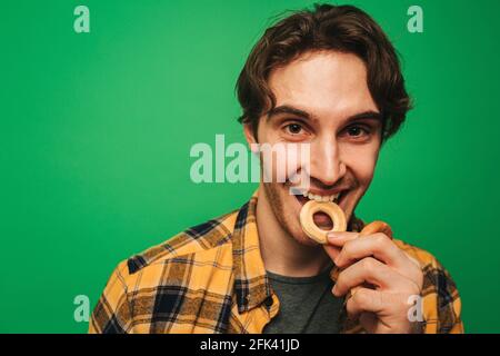 Young man enjoys eating cookie, isolated on green background Stock Photo