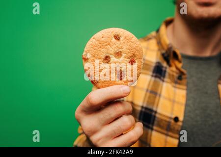 Close up young man holds cookie, isolated on green background Stock Photo