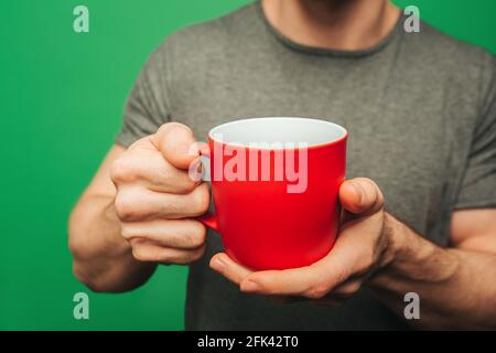 Close up man is holding cup of tea, isolated on green background Stock Photo