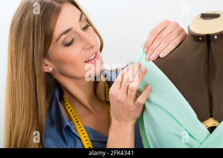 Freelancer - Fashion designer or Tailor working on a design or draft, she takes measure on a dressmakers dummy Stock Photo