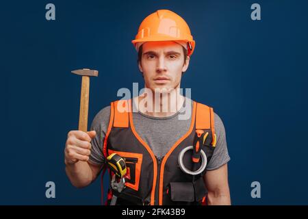 Serious builder in a helmet with a hammer, isolated over blue background Stock Photo