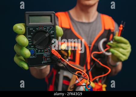 Close up builder is holding digital multimetert in gloves, isolated over blue background Stock Photo