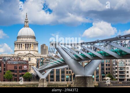 View of St. Paul's Cathedral and the Millennium Bridge, taken from the south side of the Thames River embankment on a sunny day with puffy clouds.