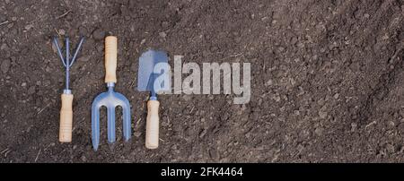 Hand garden tools on black fertile soil. Preparation for planting seedlings. Banner panorama Stock Photo