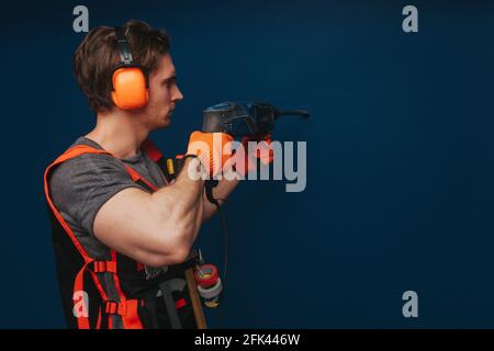 Young builder is drilling the wall, isolated over blue background Stock Photo