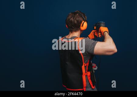 Young builder is drilling the wall, isolated over blue background Stock Photo