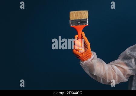 Builder's hand is holding paint brush, isolated over blue background Stock Photo