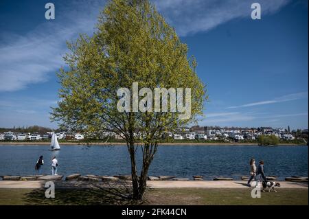 Dortmund, Germany. 28th Apr, 2021. Strollers and a sailboat are out and about at Phoenix Lake. Credit: Bernd Thissen/dpa/Alamy Live News Stock Photo