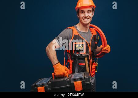 Happy young builder is happy with equipments, isolated on blue background. Stock Photo
