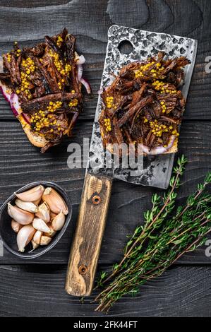 Pulled pork Sandwich with smoked pork meat on a meat cleaver. Black wooden background. Top view Stock Photo