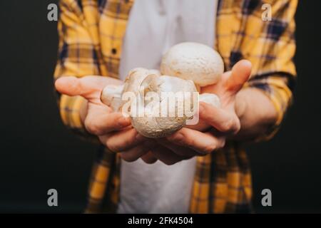 Close up of young blond man in yellow shirt is holding mushrooms in hands with smile, isolated over black background Stock Photo