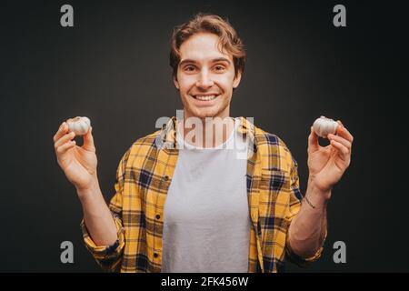 Young blond man in yellow shirt is holding garlics in both hands, isolated over black background Stock Photo
