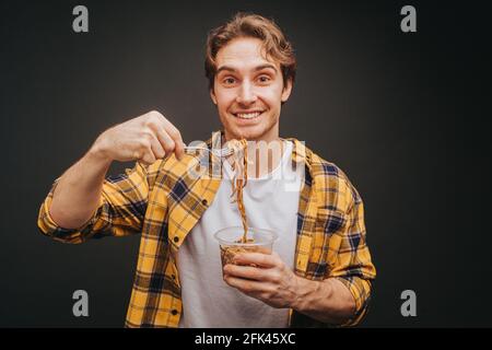 Young blond man in yellow shirt smiling and holding spaghetti fork , isolated over black background Stock Photo