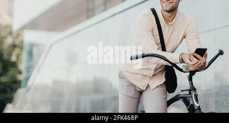 Young businessman walking outdoors with bicycle and using mobile phone, going to work on bike Stock Photo