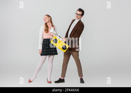 man holding vintage tape recorder near joyful woman standing with closed eyes on grey Stock Photo