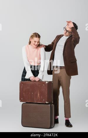 young woman laughing near suitcases and tired boyfriend on grey background Stock Photo