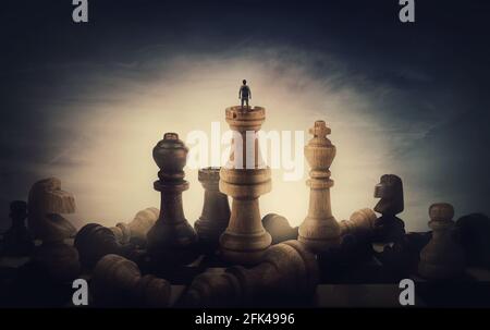 Chess player achieving success. Surreal and conceptual scene of a tiny person standing on the top of chessboard among huge chess pieces. Overcoming ob Stock Photo