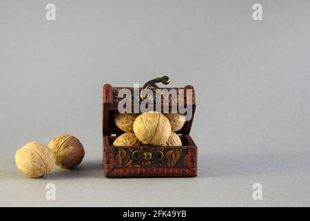 Small chest full of walnuts on gray background. Side lighting. Close-up. Selective focus. Copy space. Stock Photo