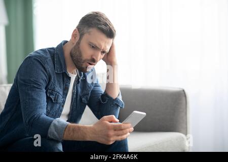 Closeup of thoughtful man sitting on couch, using smartphone Stock Photo