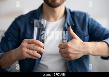 Unrecognizable man holding glass of water and showing thumb up Stock Photo