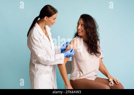 Doctor Vaccinating Patient Sticking Plaster On Vaccinated Arm Blue Background Stock Photo