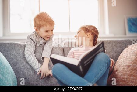 Cute children sitting on the soft sofa and reading books Stock Photo