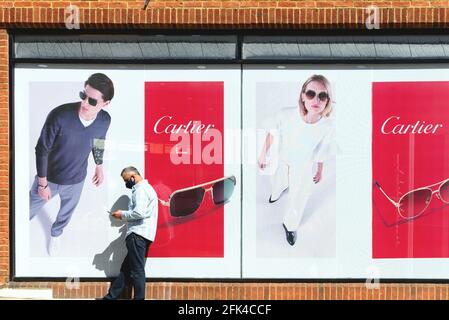 A middle aged man using a mobile phone standing outside the opticians 'Eye Academy'  with Cartier Sunglasses window display behind him Stock Photo