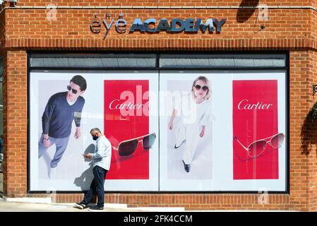 A middle aged man using a mobile phone standing outside the opticians 'Eye Academy'  with Cartier Sunglasses window display behind him Stock Photo