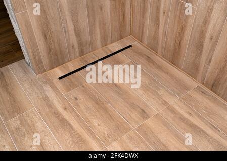Modern black linear drain in a bathroom lined with ceramic tiles imitating wood. Stock Photo