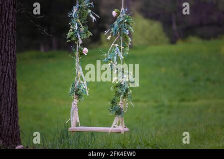 A flower decorated swing hangs from a tree. Stock Photo