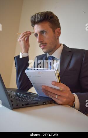 Spanish businessman looking at his laptop while checking on his calendar notebook Stock Photo