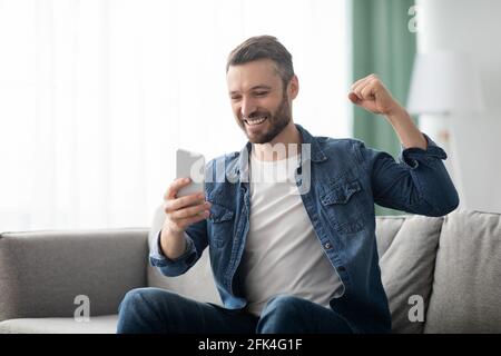 Emotional bearded man celebrating success, using mobile phone Stock Photo