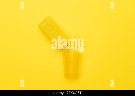 Yellow bottle pouring in a yellow cup with yellow wooden splash sign on a yellow background. Creative, abstract top view. Stock Photo