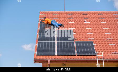 A worker installs solar panels of a power plant on the roof of a private house. Stock Photo