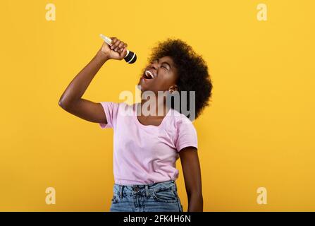 Joyful african american lady singing songs in microphone, having fun and enjoying the moment, yellow background Stock Photo