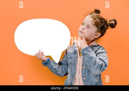 Pretty caucasian preschooler girl kid holding big empty paper mind cloud thinking over creative idea, wear denim jacket, isolated over orange wall Stock Photo