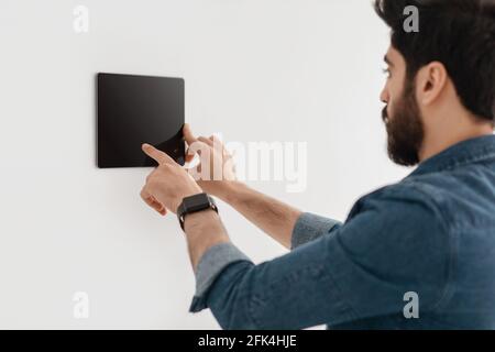 Innovative technology for apartment. Guy using digital tablet on wall with smart home control system app Stock Photo