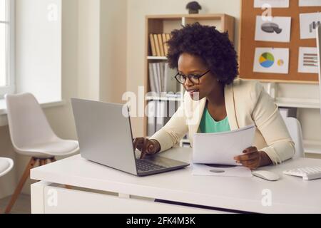 Smiling african american businesswoman focusing on preparing report in office Stock Photo