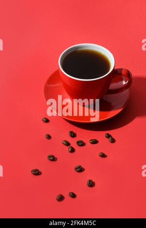 Red cup of coffee and beans on red background. Vertical format. Close up. Stock Photo