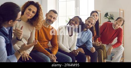 Group of interracial people sit in a row and listen with interest to a man telling his story. Stock Photo