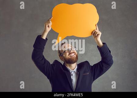 Happy young man in suit holding up orange speech bubble isolated on grey background Stock Photo