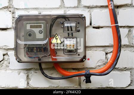 Closeup electrical power supply box with counter, fuses and switch with a transparent plastic cover on a old white brick wall Stock Photo