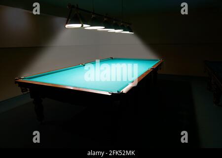 Empty billiard table with green cloth in the dark, lit by lamps from above Stock Photo