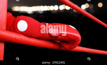 Closeup boxer hand in red glove on the ring rope. Shallow focus and dark background with blurred lights. Stock Photo