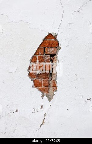 Old cracked white wall with broken plaster through which red bricks are visible Stock Photo