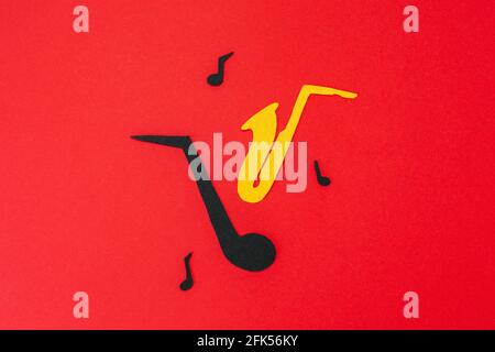 International Jazz Day. Silhouette of a saxophone and note with melodies on a red background, cutted out of felt. Flat lay. Stock Photo