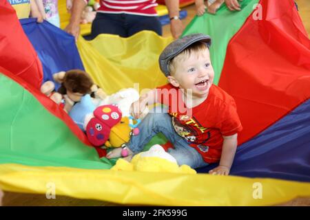 Little boy in flat cap enjoying himself in a mutli-coloured parachute Stock Photo