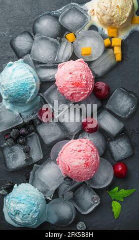Ice cream balls and berries on ice cubes on a black background. Stock Photo