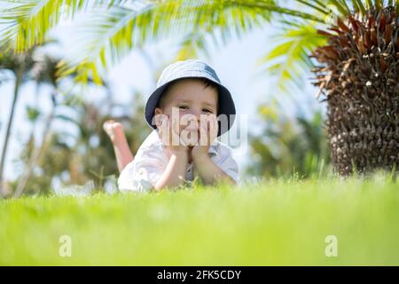 Happy little boy laying on green grass under palms Stock Photo